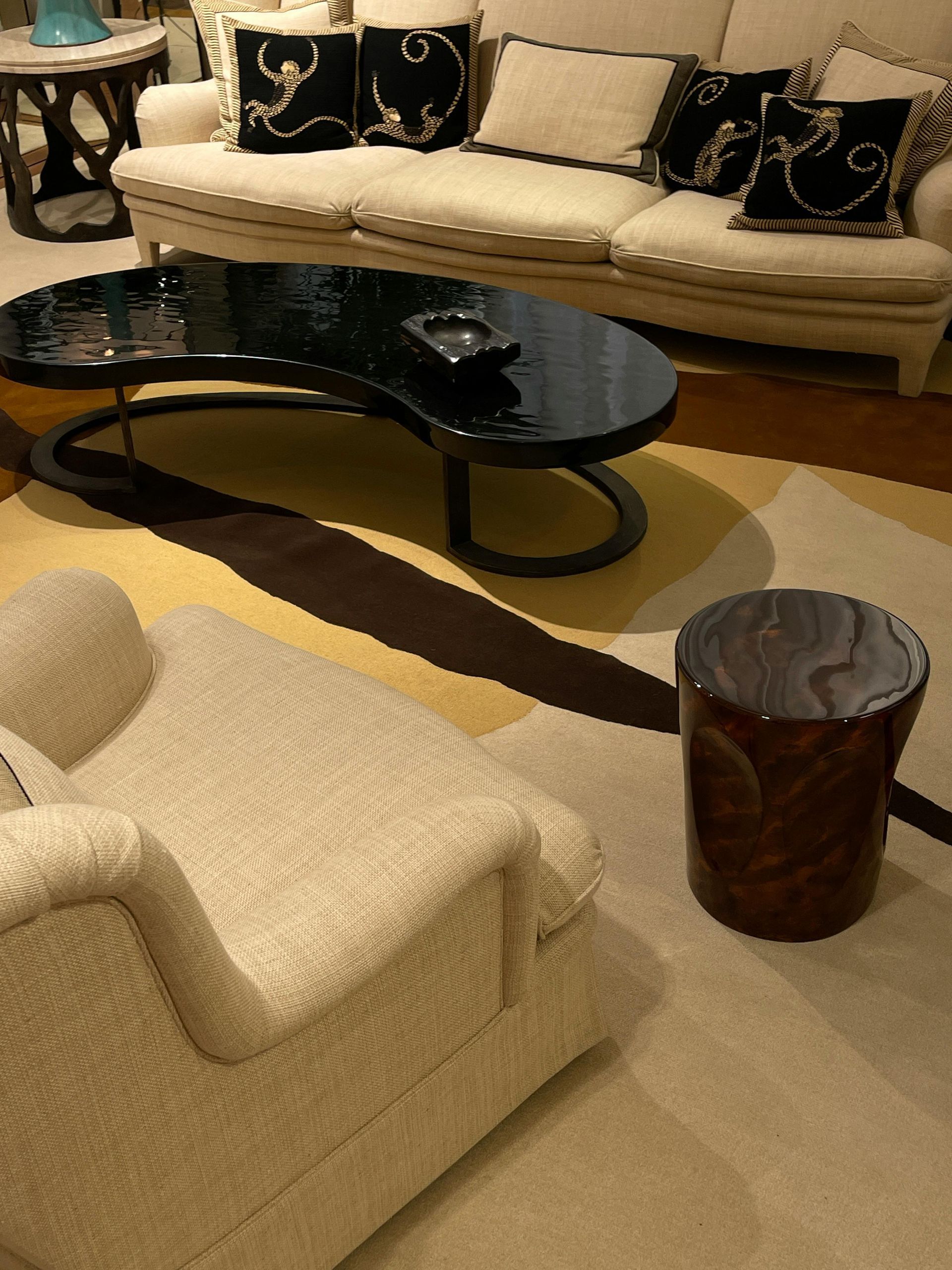 A modern living room with a white sofa, a black kidney-shaped coffee table, a textured armchair, and a dark wood stool.