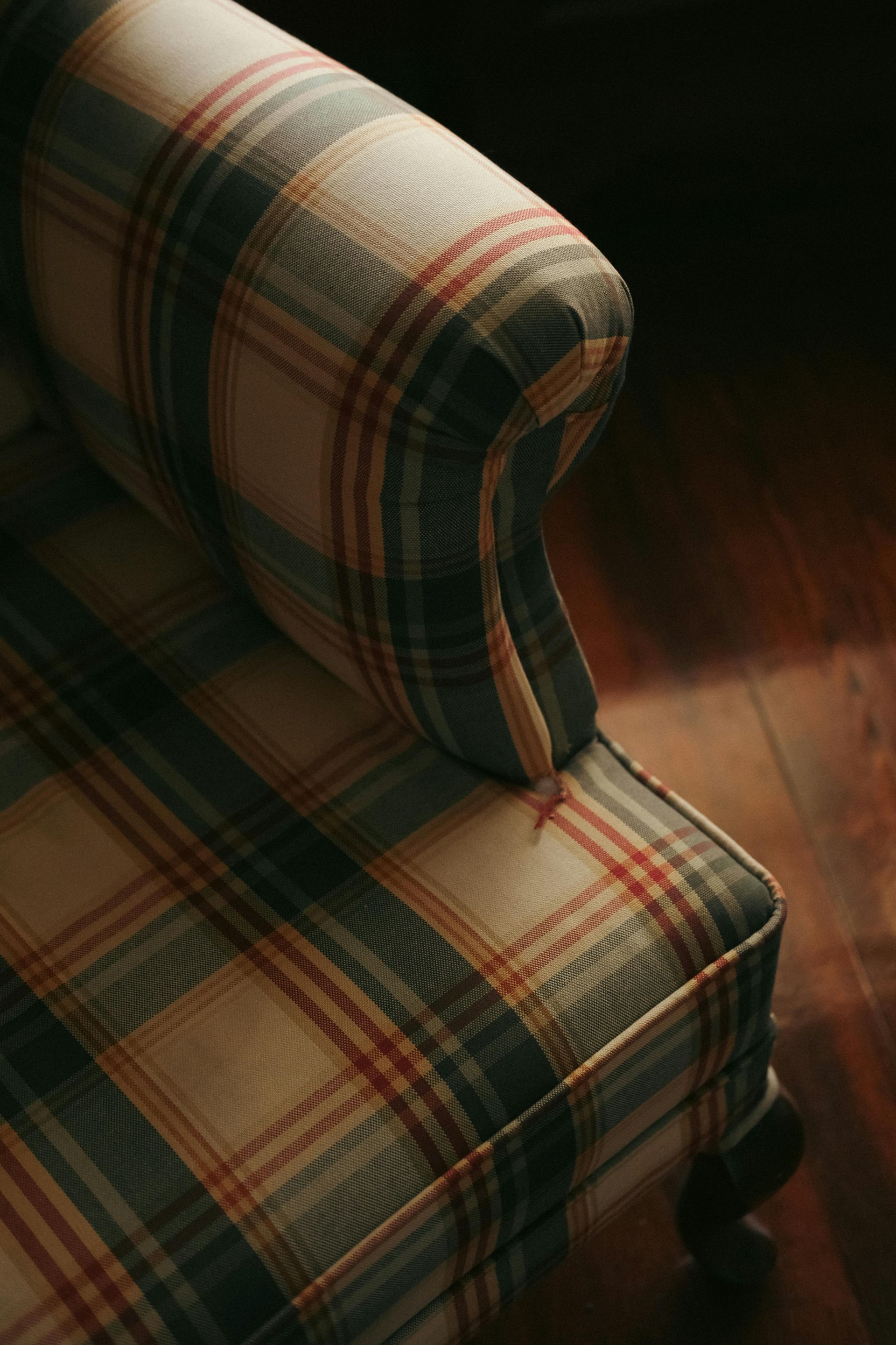 A close-up of the arm and seat of a chair upholstered in a plaid fabric with cream, green, and orange-red stripes.