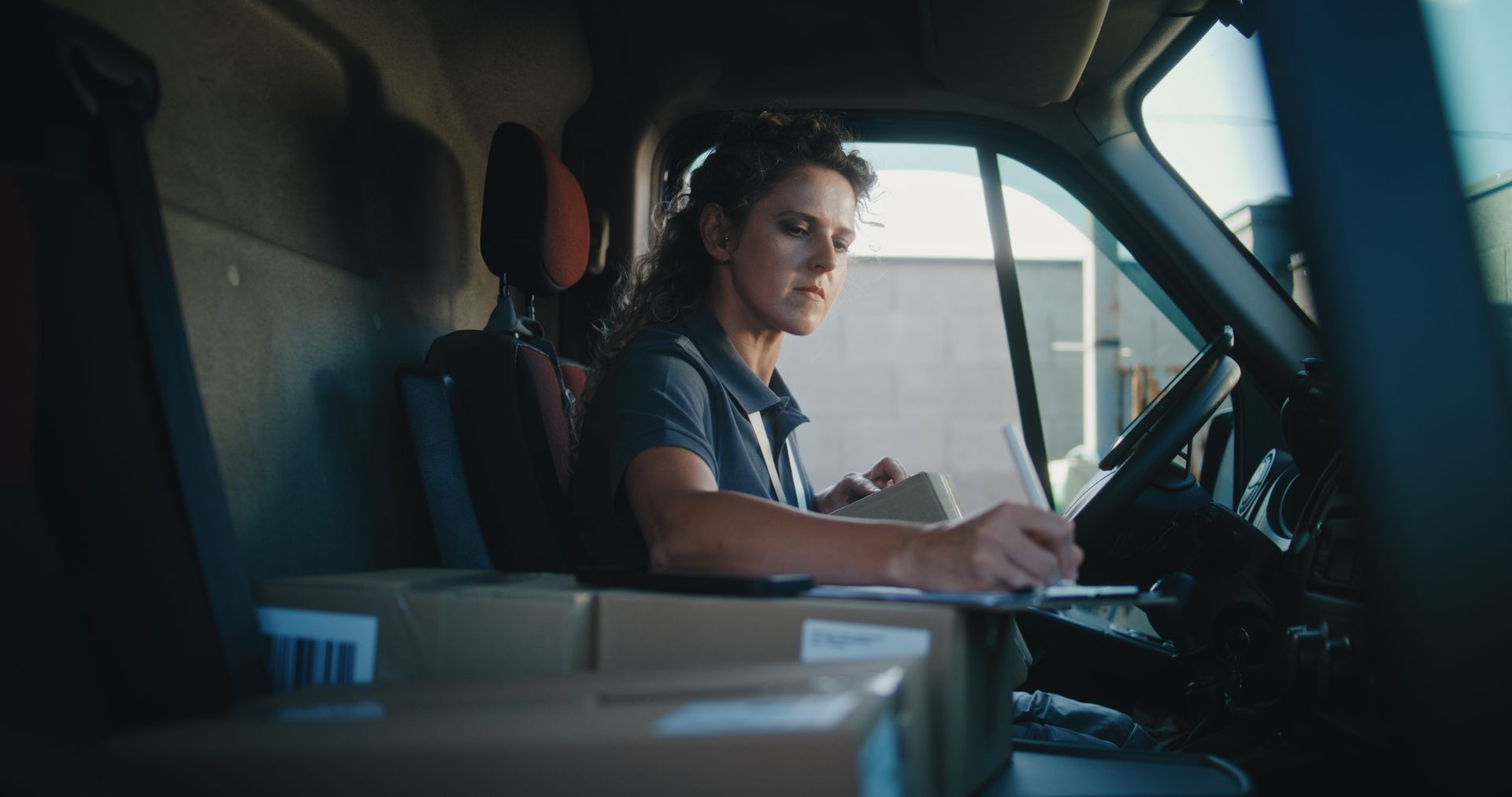 Driver's hands on steering wheel, dashboard visible, blurry city lights in background.