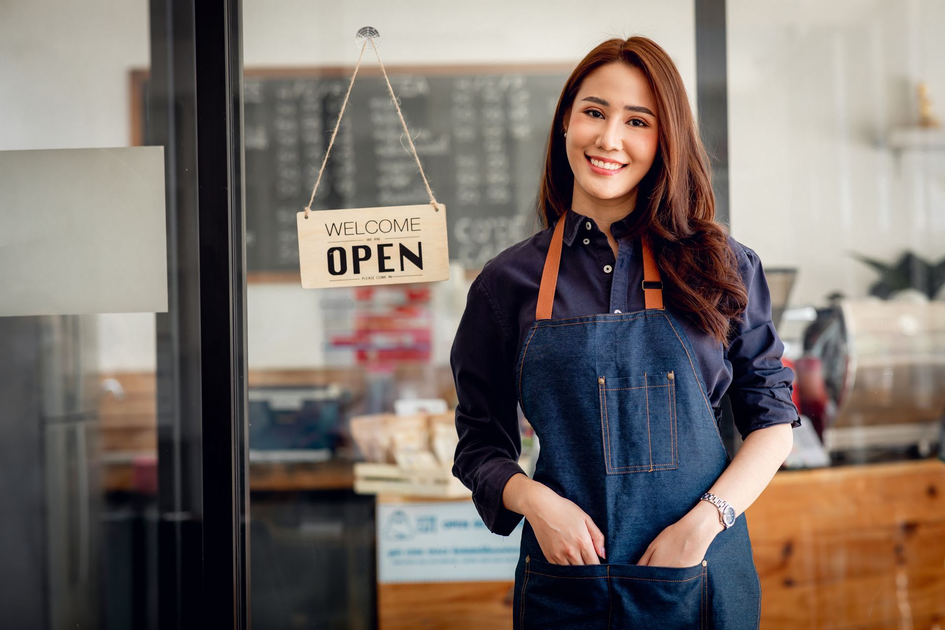 Woman on phone at a desk with laptop, clothing, and packages, smiling, in a small business setting.