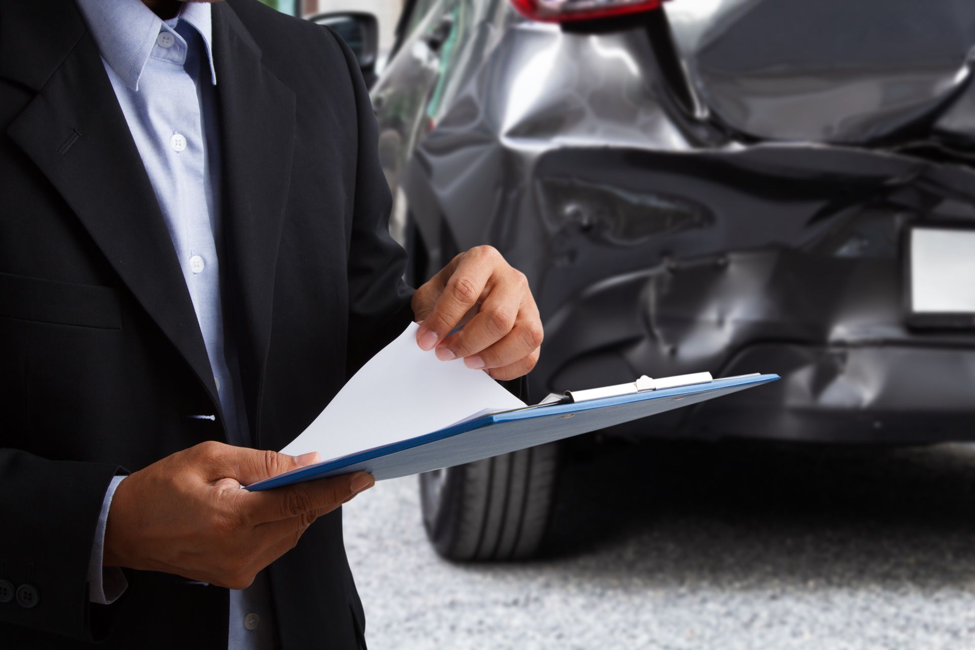 Person in suit holding clipboard, examining car damage.