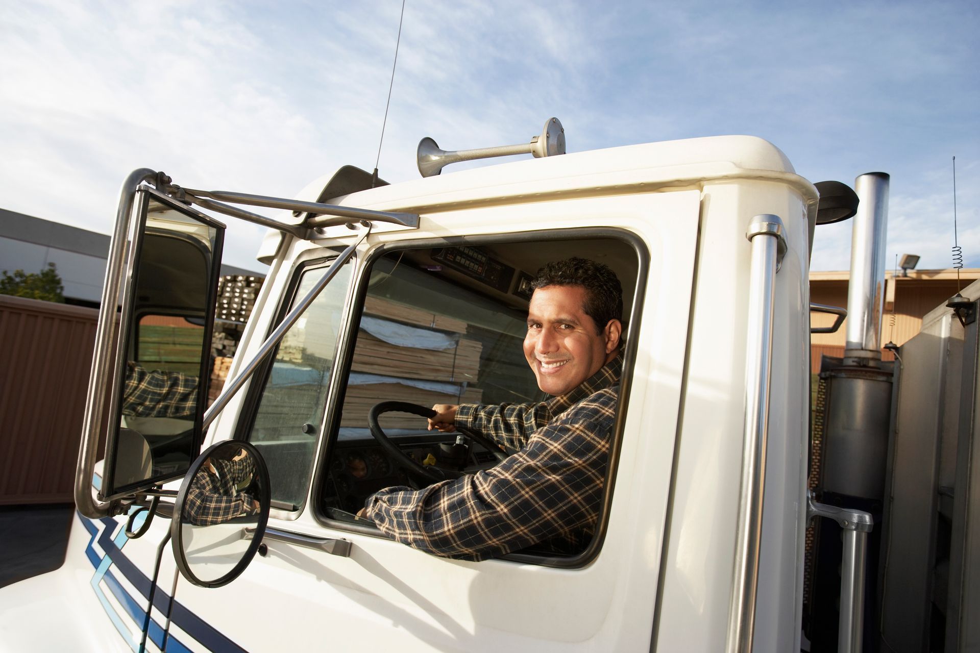 Man smiling, driving a white semi-truck with a blue stripe.