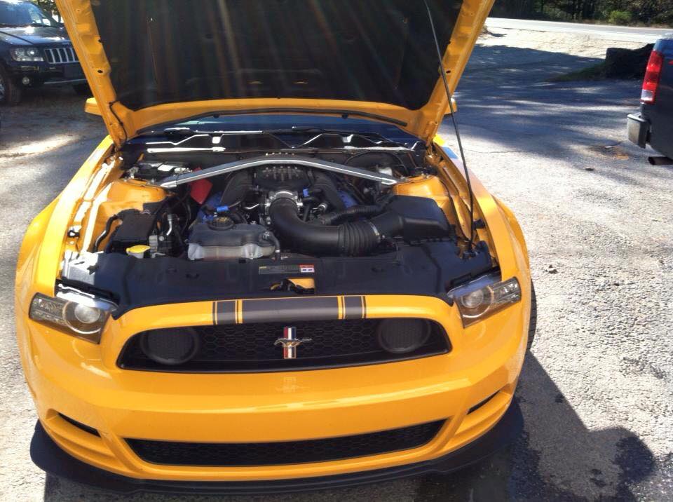 A yellow mustang with the hood up is parked in a parking lot