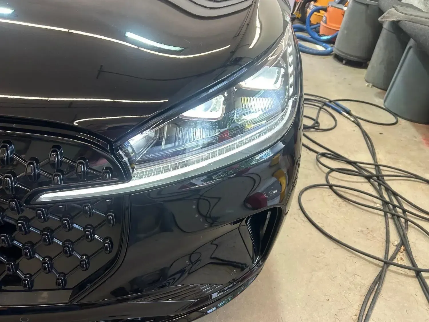 Black car front with detailed headlights and grill, indoor setting.