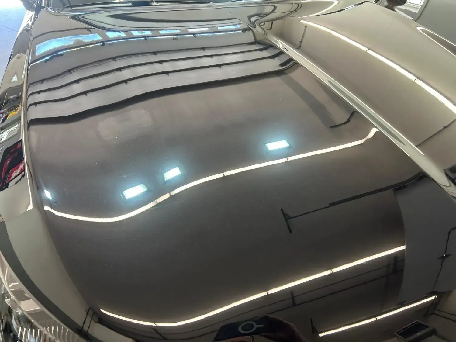 Black car hood reflecting white fluorescent lights.