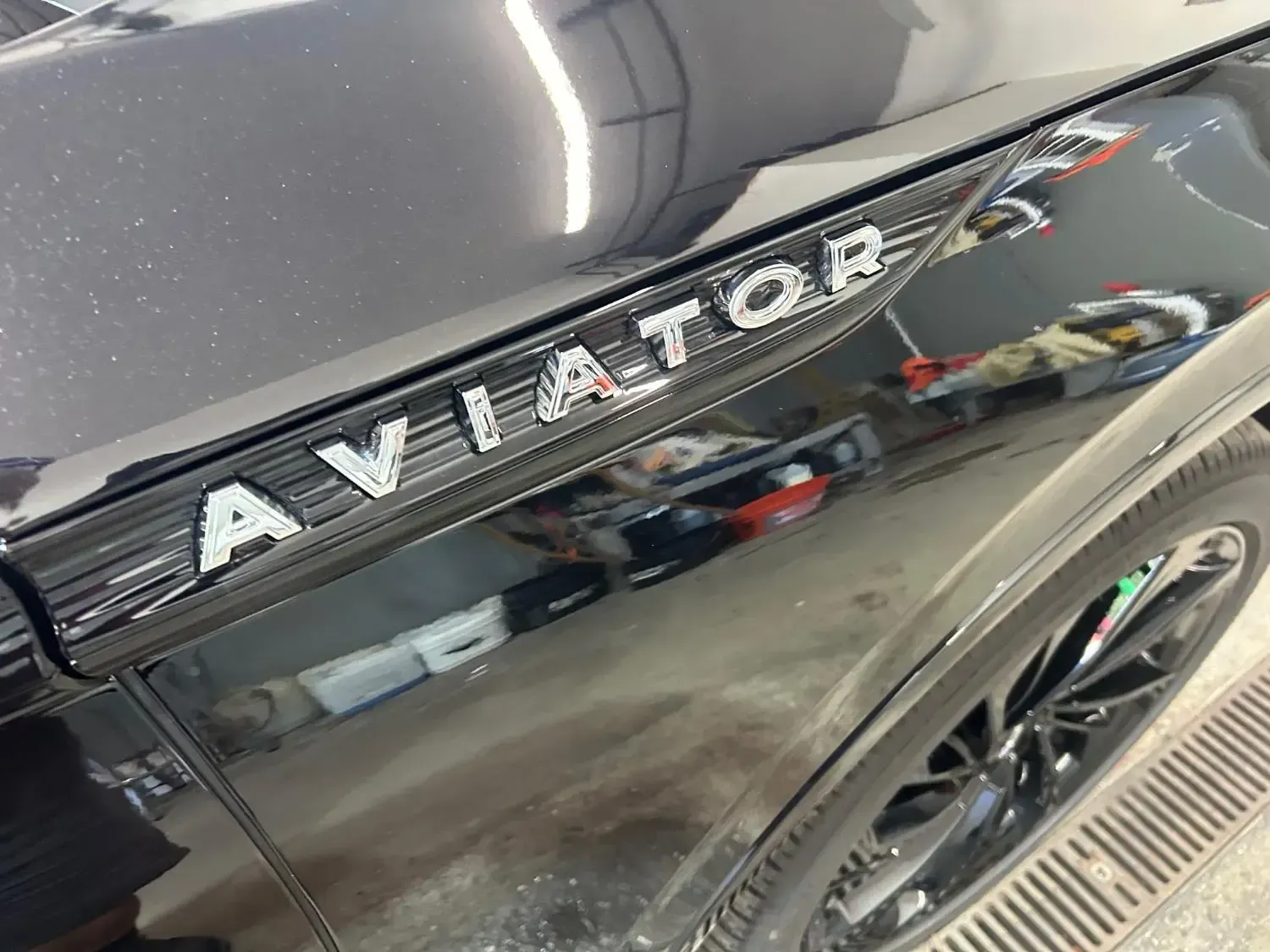 Black Lincoln Aviator emblem on a black car fender, reflecting surroundings.