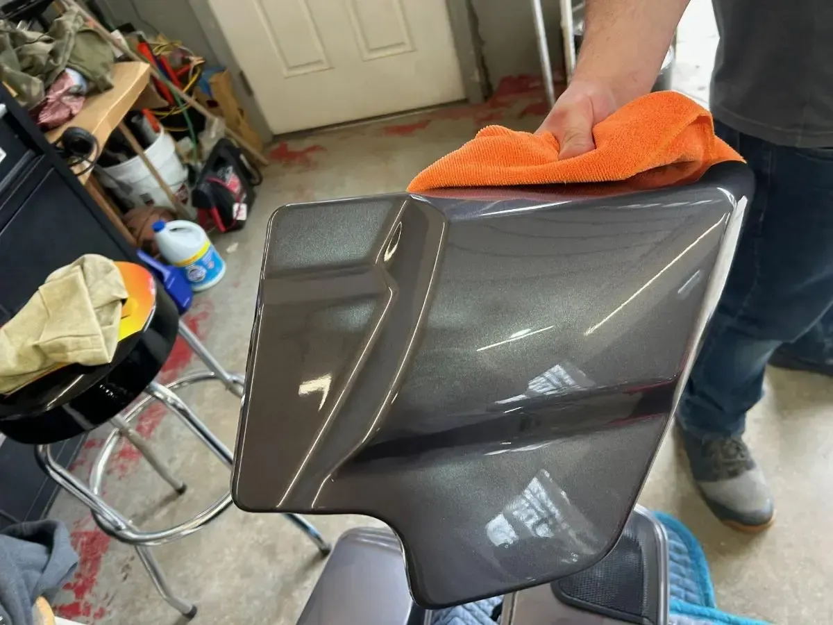 Person wiping a brown leather chair with an orange cloth in a garage
