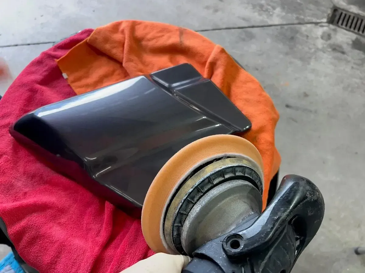 Black-and-orange wheeled bag or scooter part on a pink towel outdoors on concrete