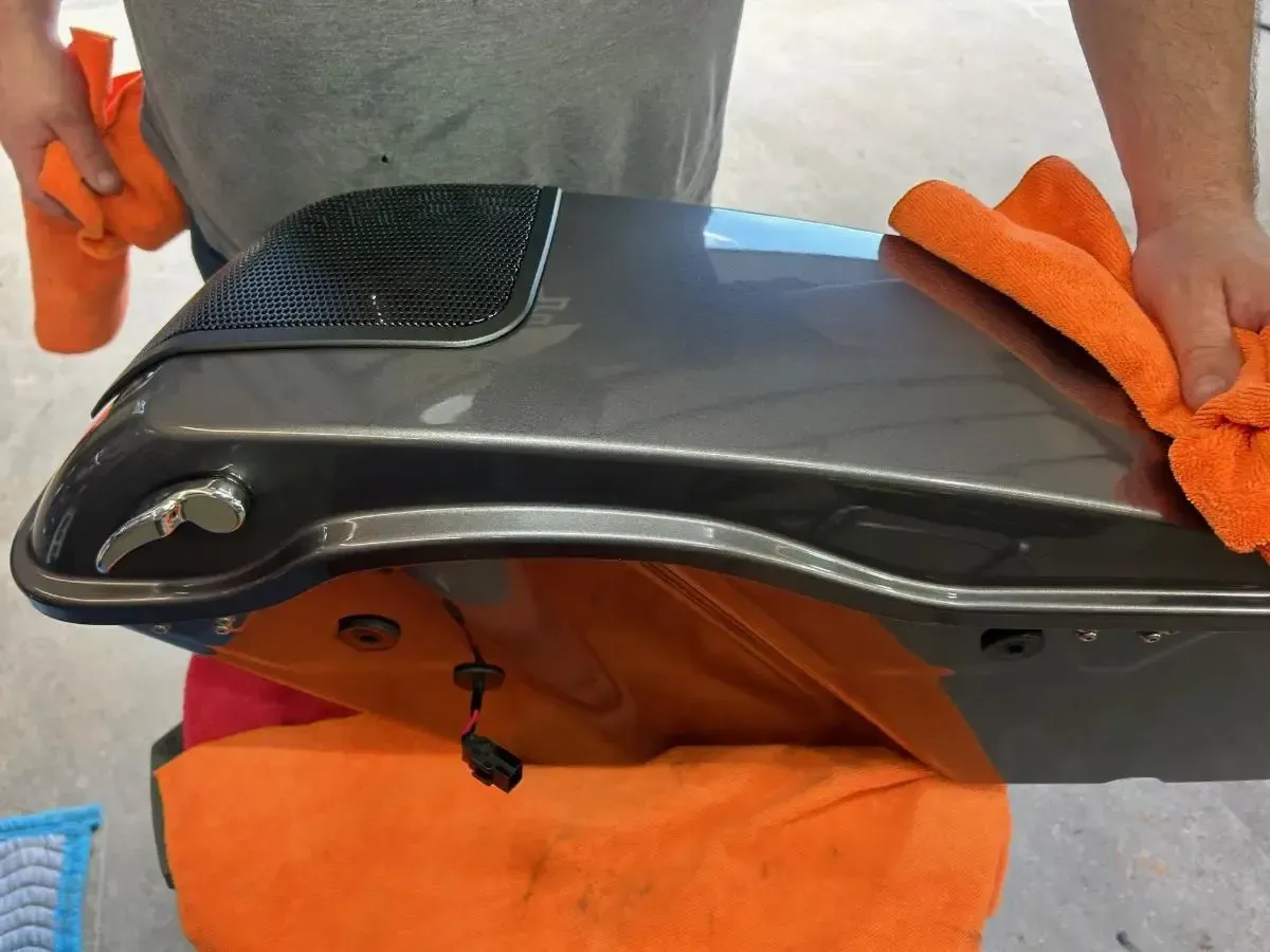 Orange-gloved hands cleaning the underside of a black appliance on an orange cloth