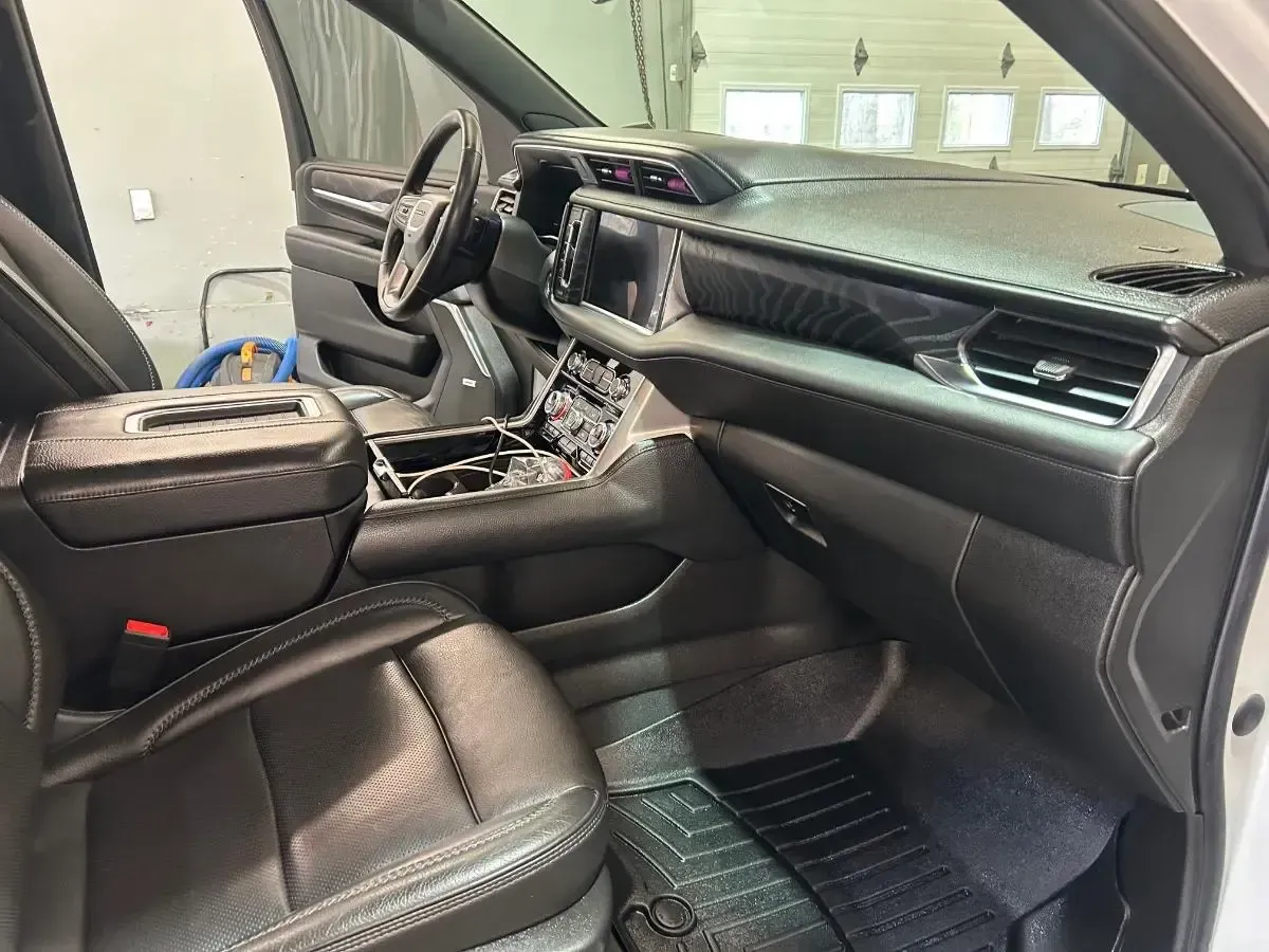 Black leather car interior with driver seat, dashboard, and open door in a garage