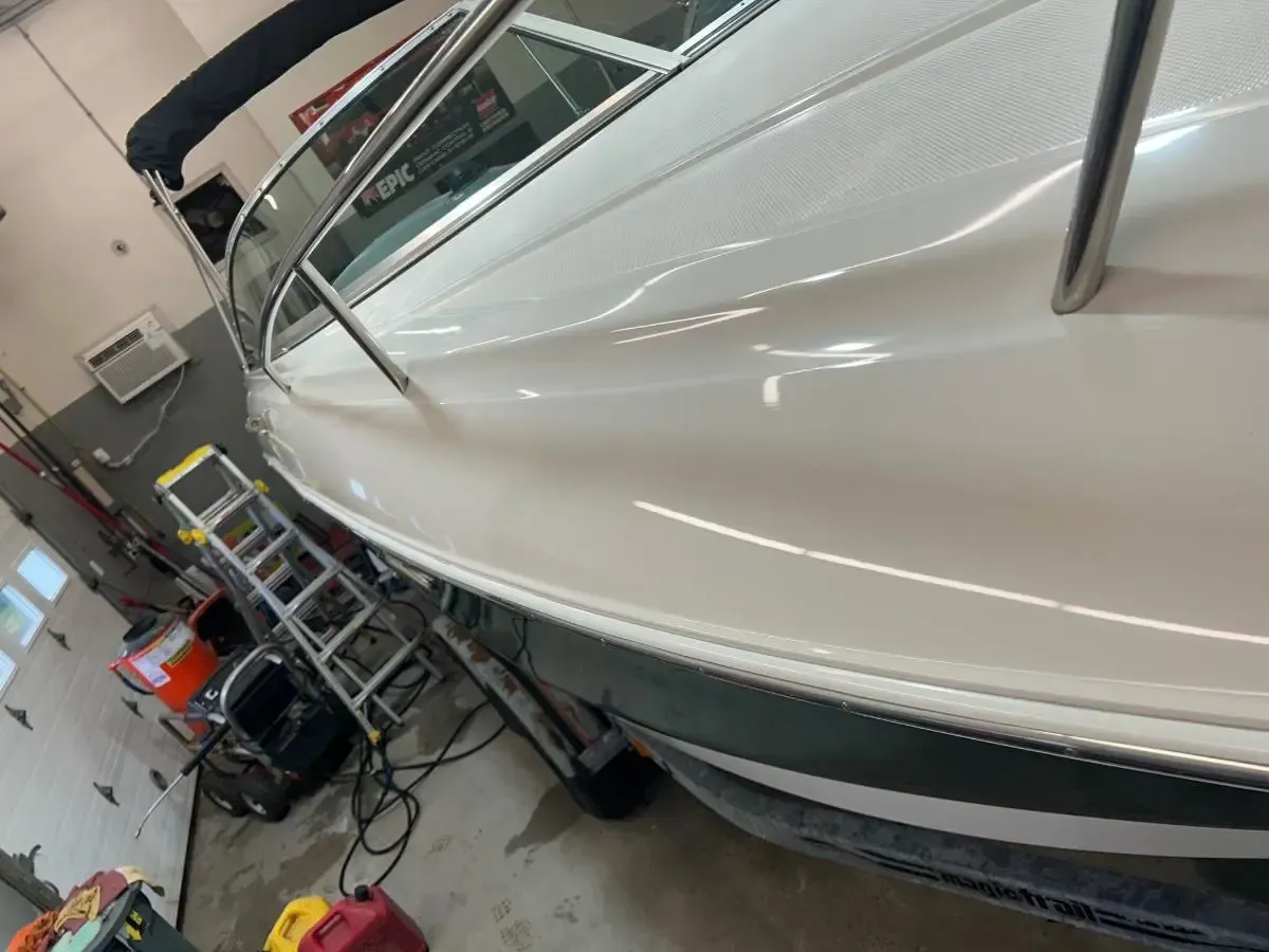 White car in an auto body shop, viewed from the side on a lift with tools nearby.