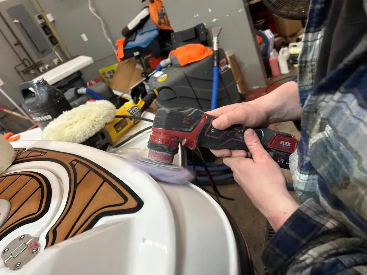 Person using a red cordless drill to work on a white vehicle in a garage.