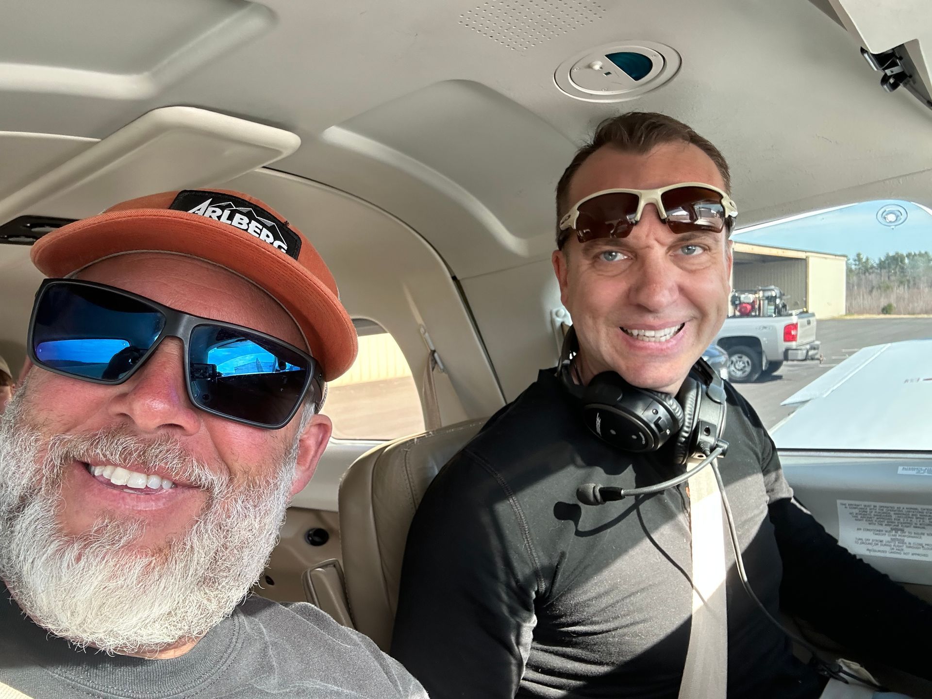 Two men wearing sunglasses and headphones are sitting in a car.