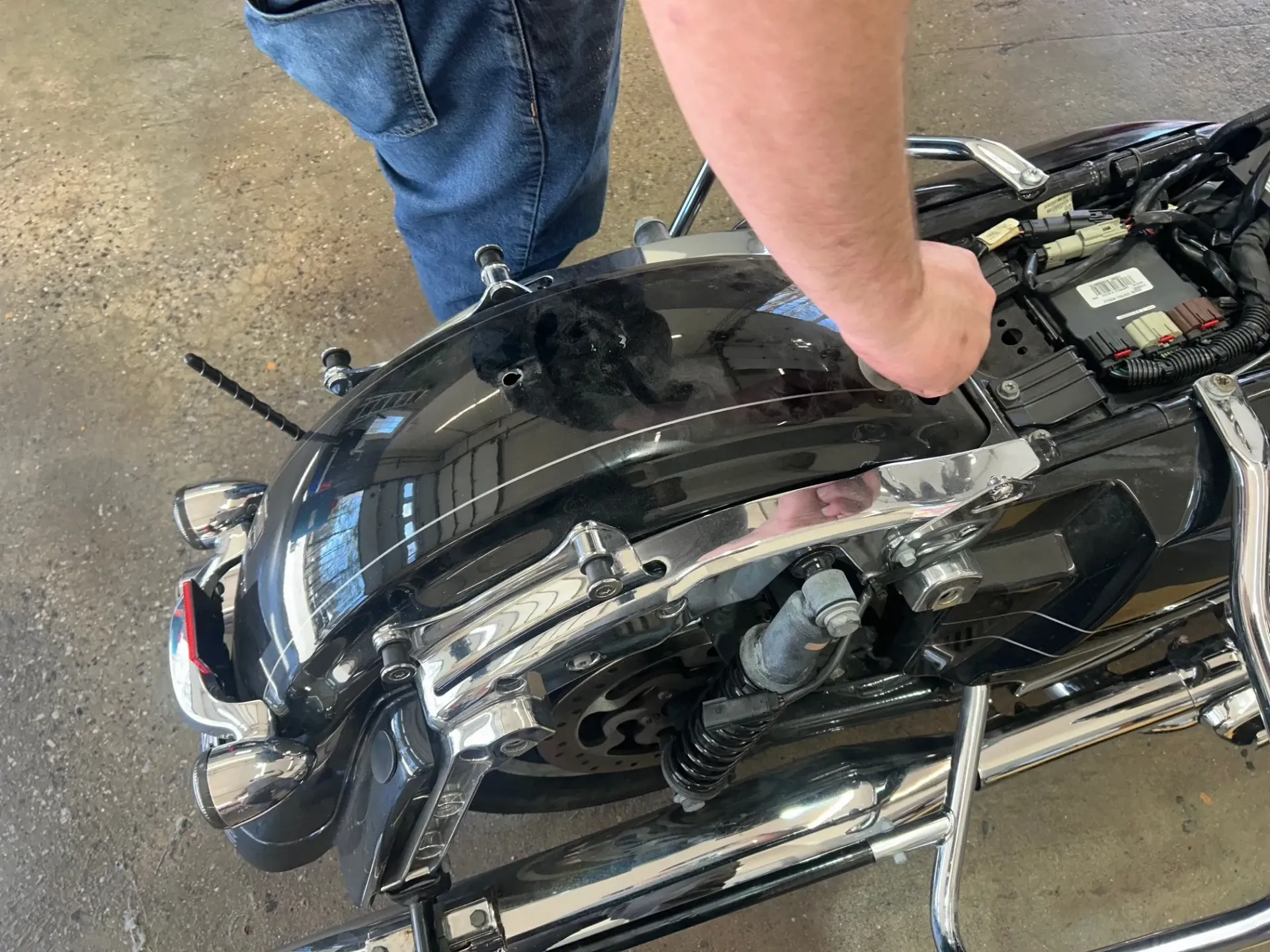 Person working on a black motorcycle in a garage, viewed from above.