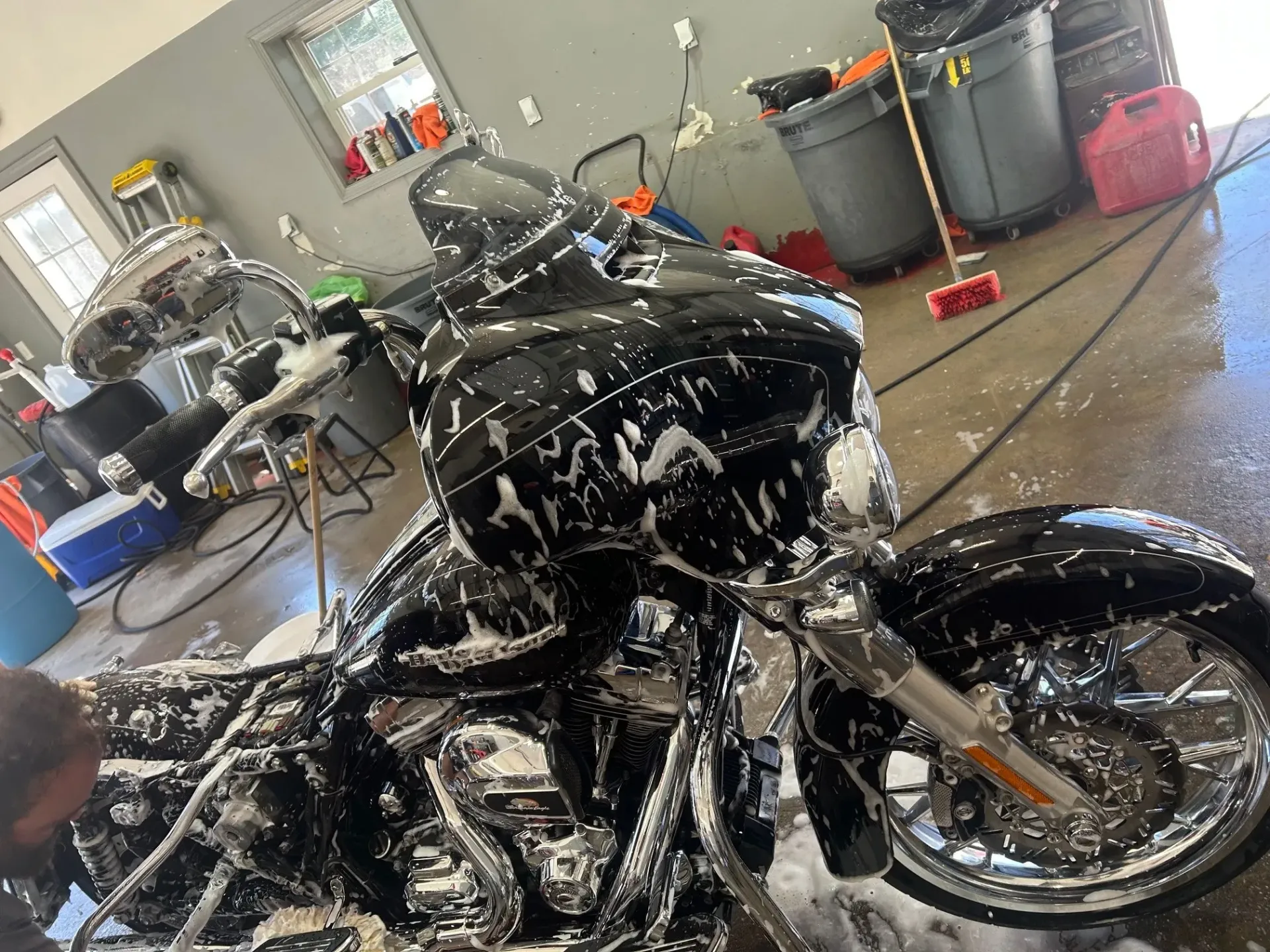 Black motorcycle covered in soap foam inside a garage, being washed by a person off-frame