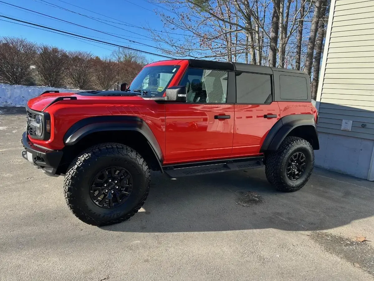 Red Ford Bronco SUV with black accents and large off-road tires, parked outdoors on a sunny day.
