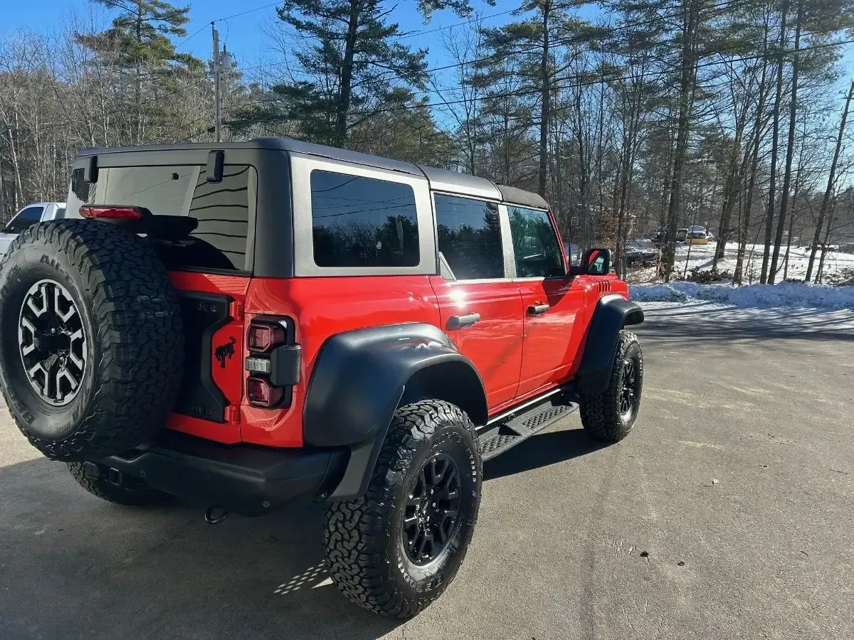 Red Ford Bronco SUV with black wheels on snowy pavement.