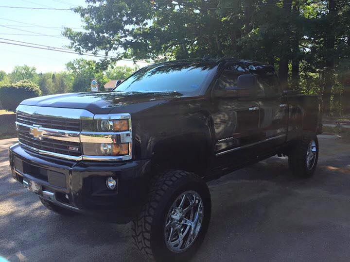 A black truck is parked in a driveway next to trees.