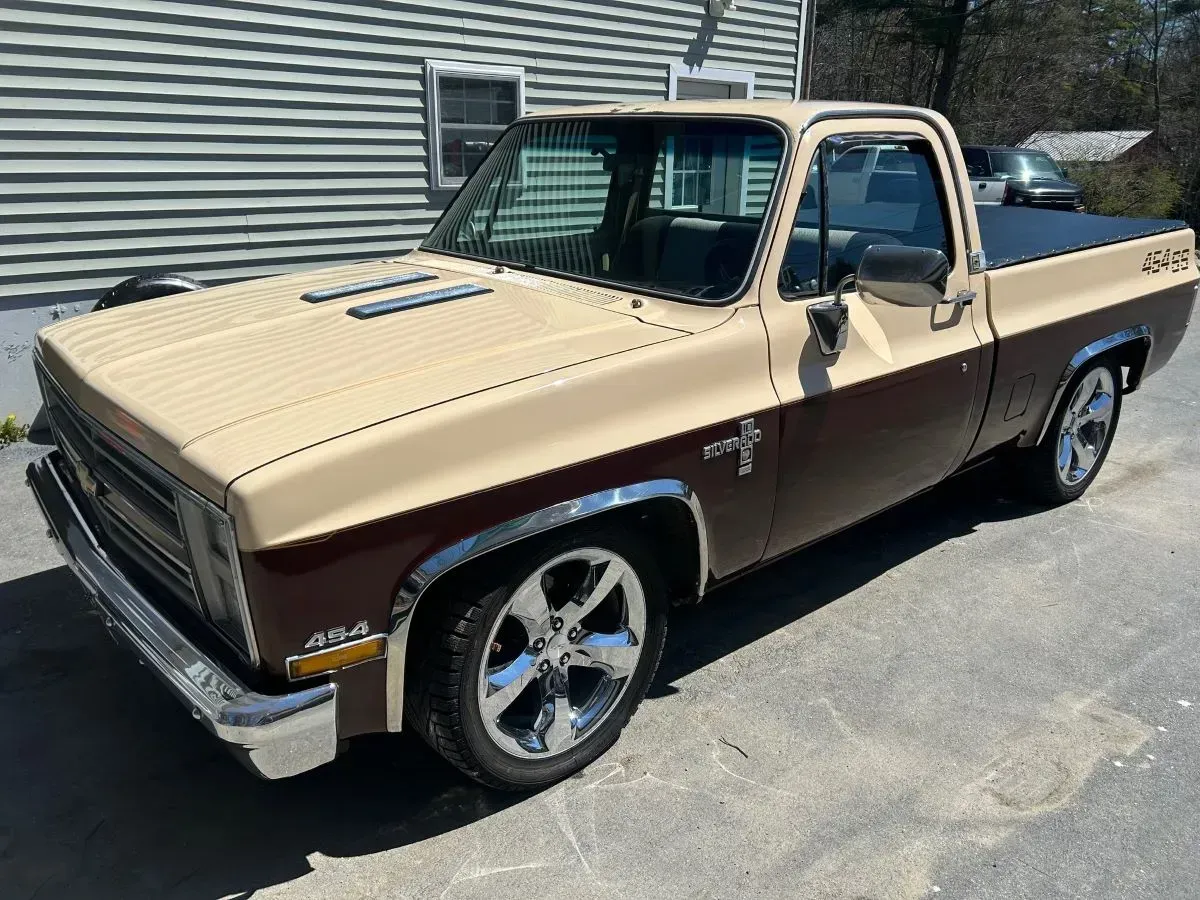 A brown and tan pickup truck is parked in front of a house.
