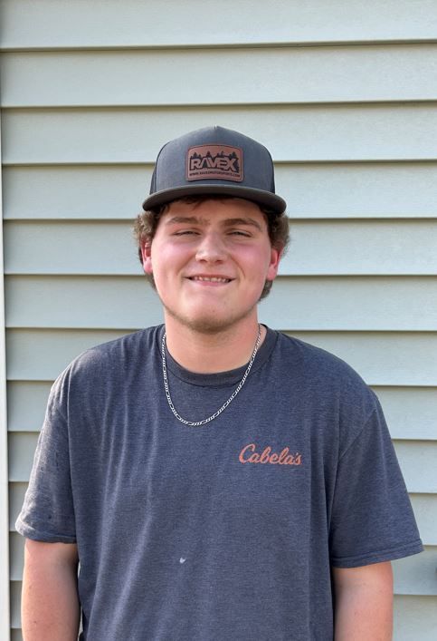 A young man wearing a hat and a t-shirt is standing in front of a house.
