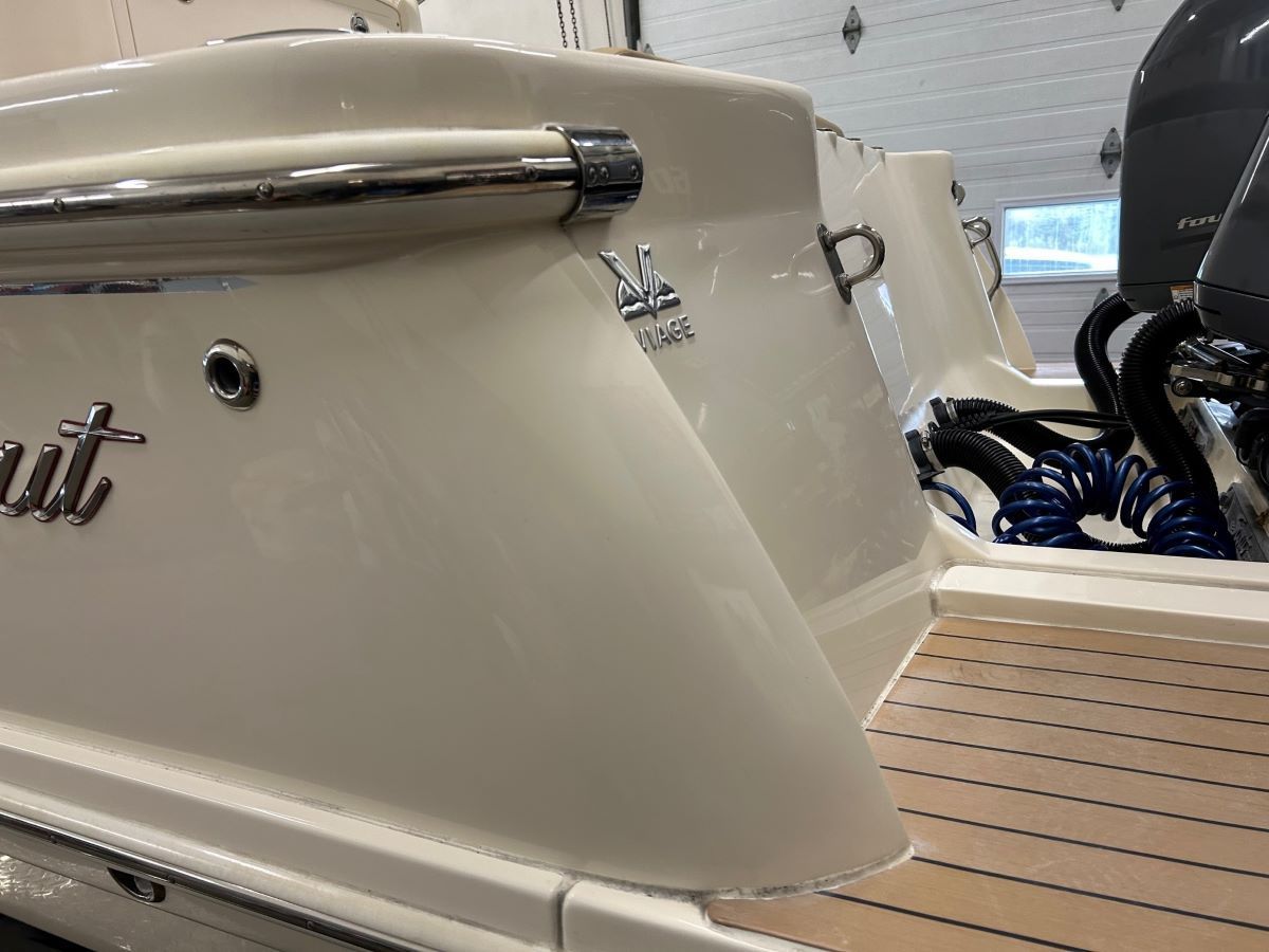 A white boat with a wooden deck is parked in a garage.