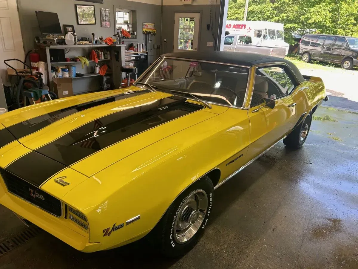 Yellow and black vintage Camaro sports car with black stripes. Parked in a garage setting.