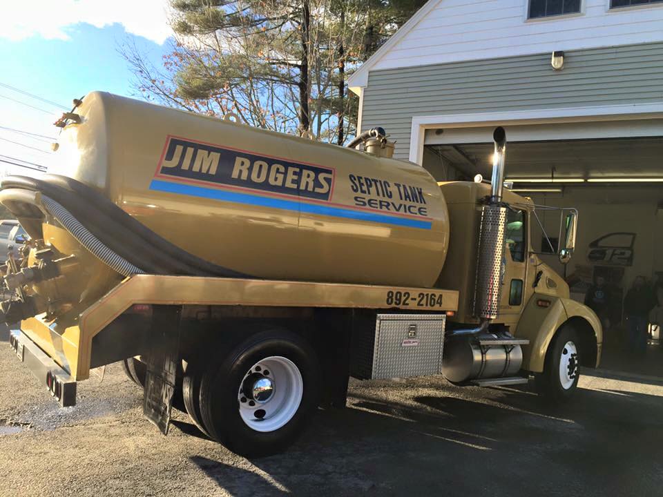A jim rogers septic tank service truck is parked in front of a garage