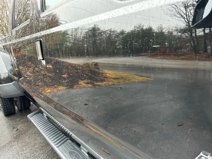 A black truck is parked on the side of the road in a parking lot.