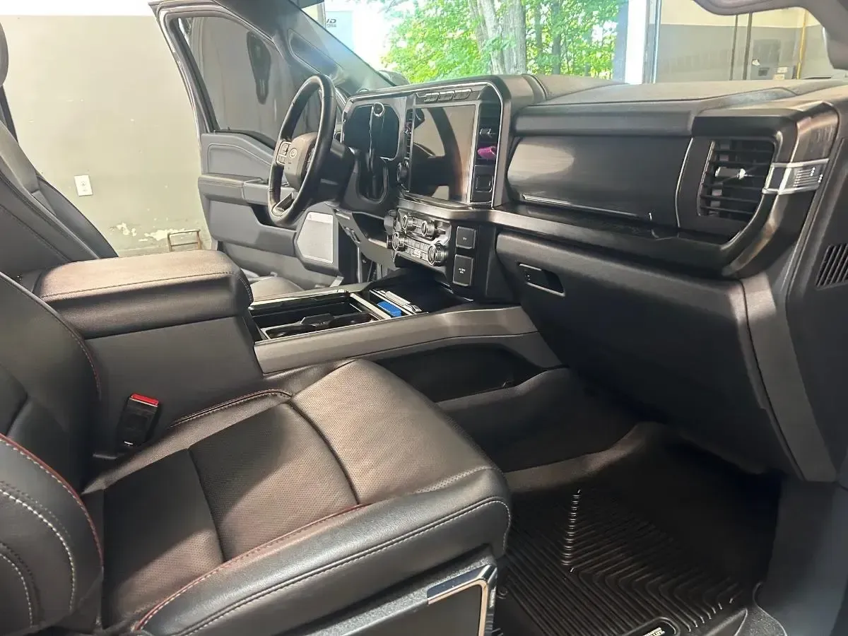 Interior of a black truck with black leather seats, dashboard, and steering wheel. Driver's side door is open.