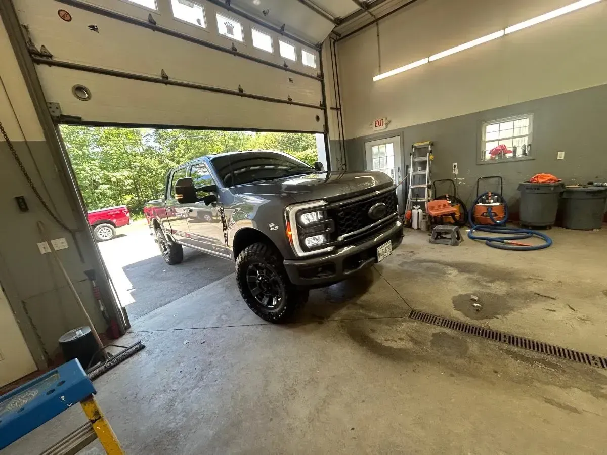 Gray Ford pickup truck in a garage bay, partially outside.