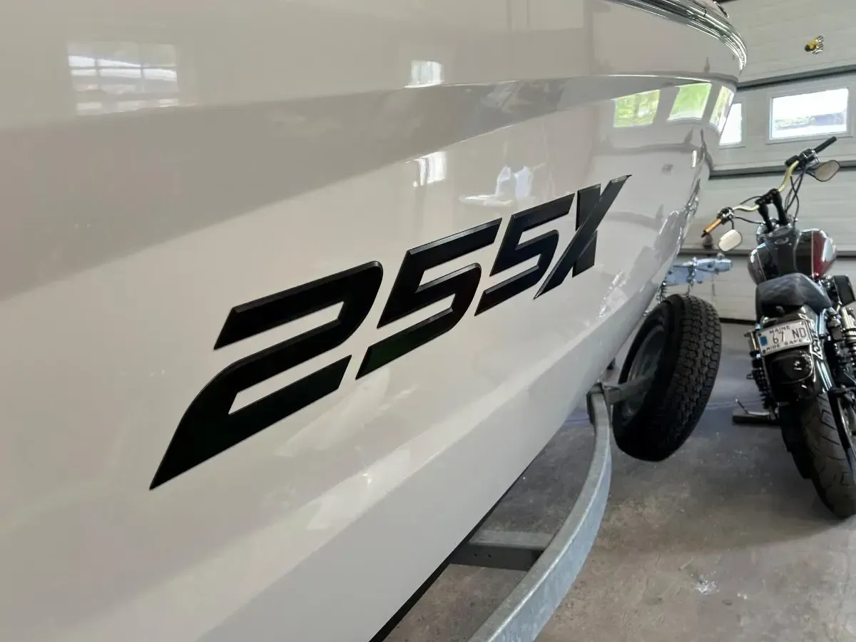 Black “255X” lettering on the side of a white boat in a garage, with two motorcycles nearby