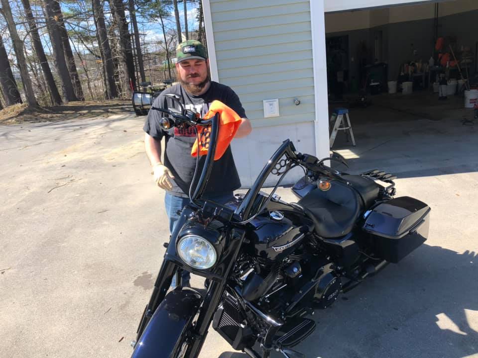 A man is standing next to a black motorcycle in a parking lot.