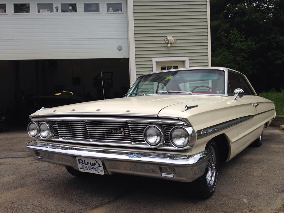 A white ford car is parked in front of a garage