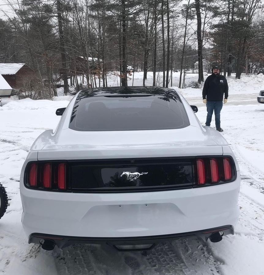 A man is standing next to a white mustang in the snow