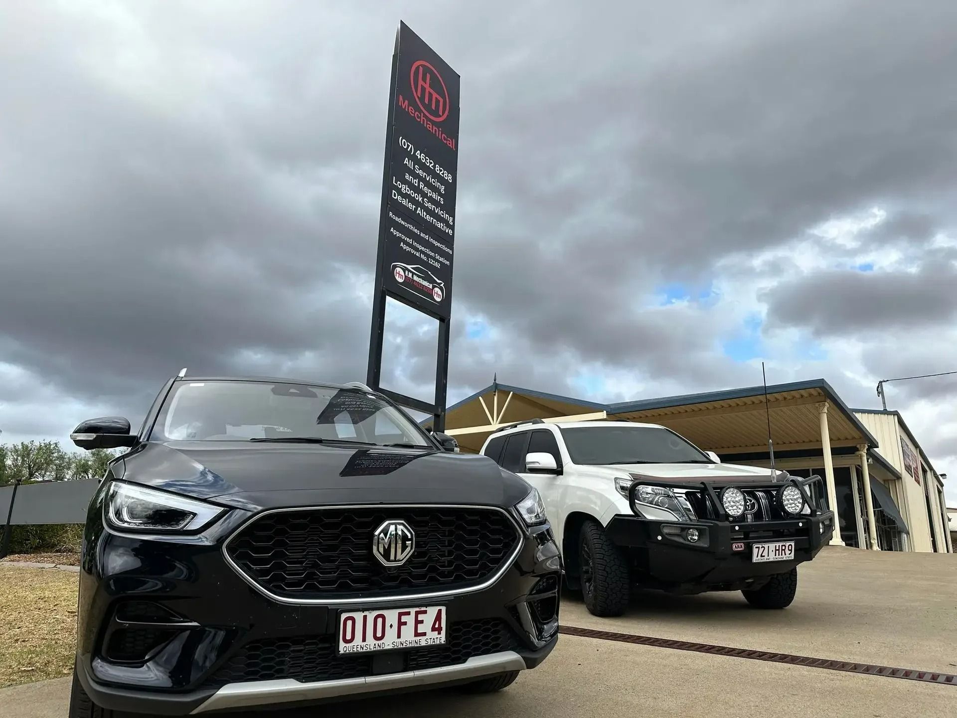 Two Cars Are Parked Next to Each Other in Front of a Building of a Mechanic Shop — H.M. Mechanical in Westbrook, QLD