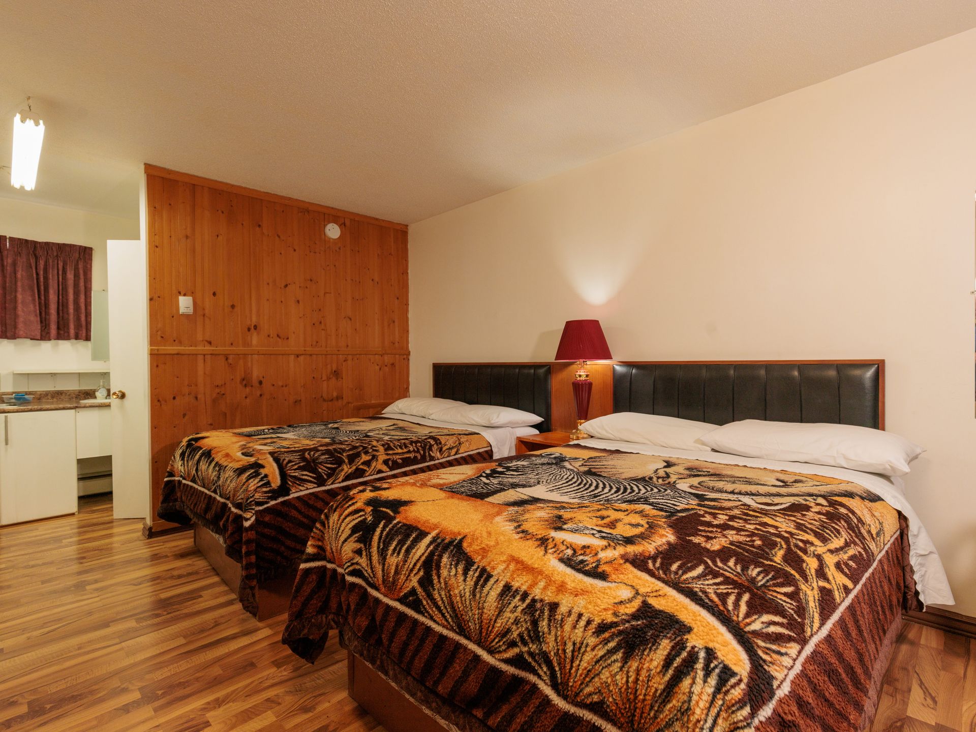A bedroom with two beds featuring animal-print blankets, a wood-paneled wall, and a lamp between the beds.