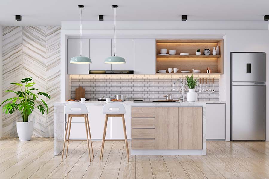 Modern kitchen with white cabinets, light wood island, two stools, stainless steel fridge, and a potted plant.