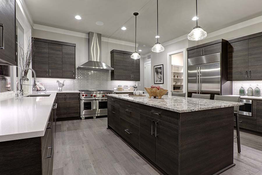 Modern kitchen with dark wood cabinetry, a large marble-topped island, stainless steel appliances, and pendant lighting.
