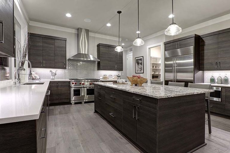 Modern kitchen with dark wood cabinetry, a large marble-topped island, stainless steel appliances, and pendant lighting.