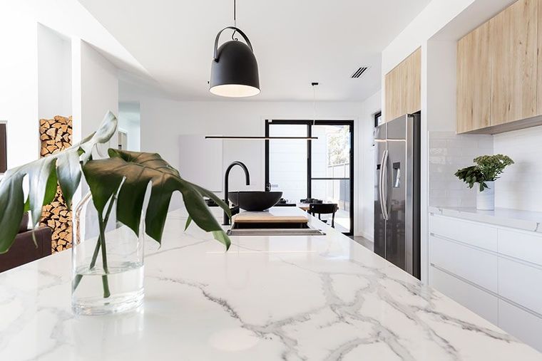 Modern kitchen with a white marble island, black pendant light, matte black faucet, and light wood upper cabinets.