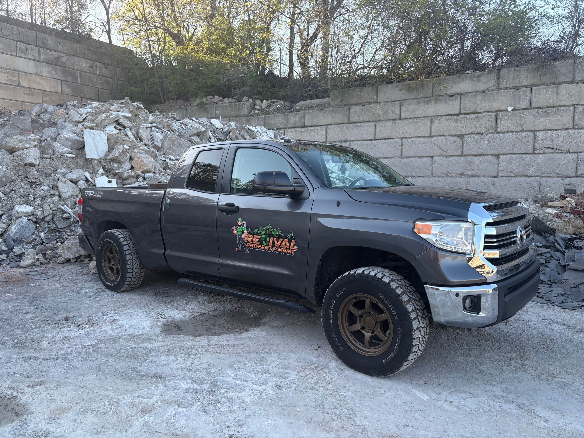 A Toyota tundra truck is parked in front of a pile of rocks and debris. Revival Property MGMT is able to haul heavy loads and get the Job done.