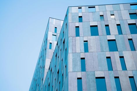 Edifício moderno com fachada de painéis e janelas em vidro azul, ideal para aplicação de películas arquitetônicas para controle solar e privacidade.