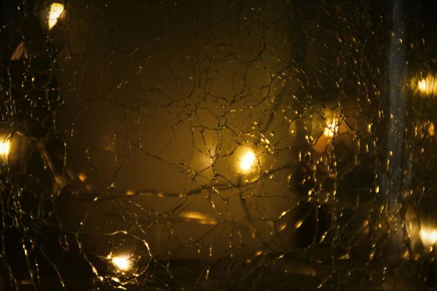Vidro com película de segurança estilhaçado refletindo luz amarela, mantendo fragmentos unidos e preservando a integridade do ambiente.