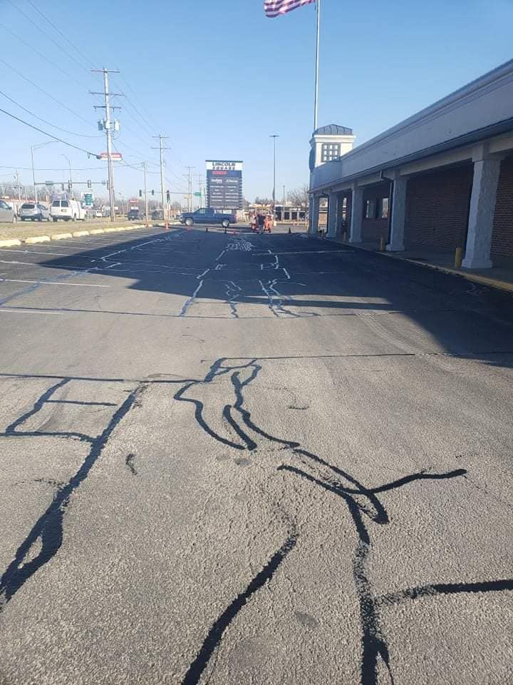 A cracked asphalt road in front of a building with a flag in the background.