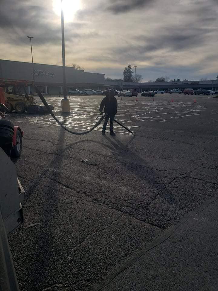 A man is standing in a parking lot holding a hose.
