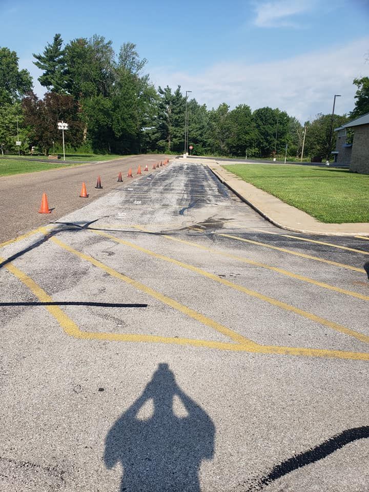 A shadow of a person is cast on the asphalt of a parking lot.