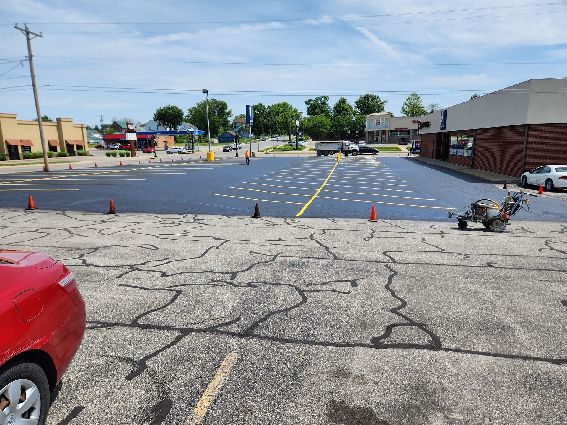 A red car is parked in a parking lot next to a building.
