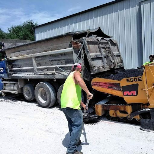 A man is pushing a shovel in front of a dump truck.