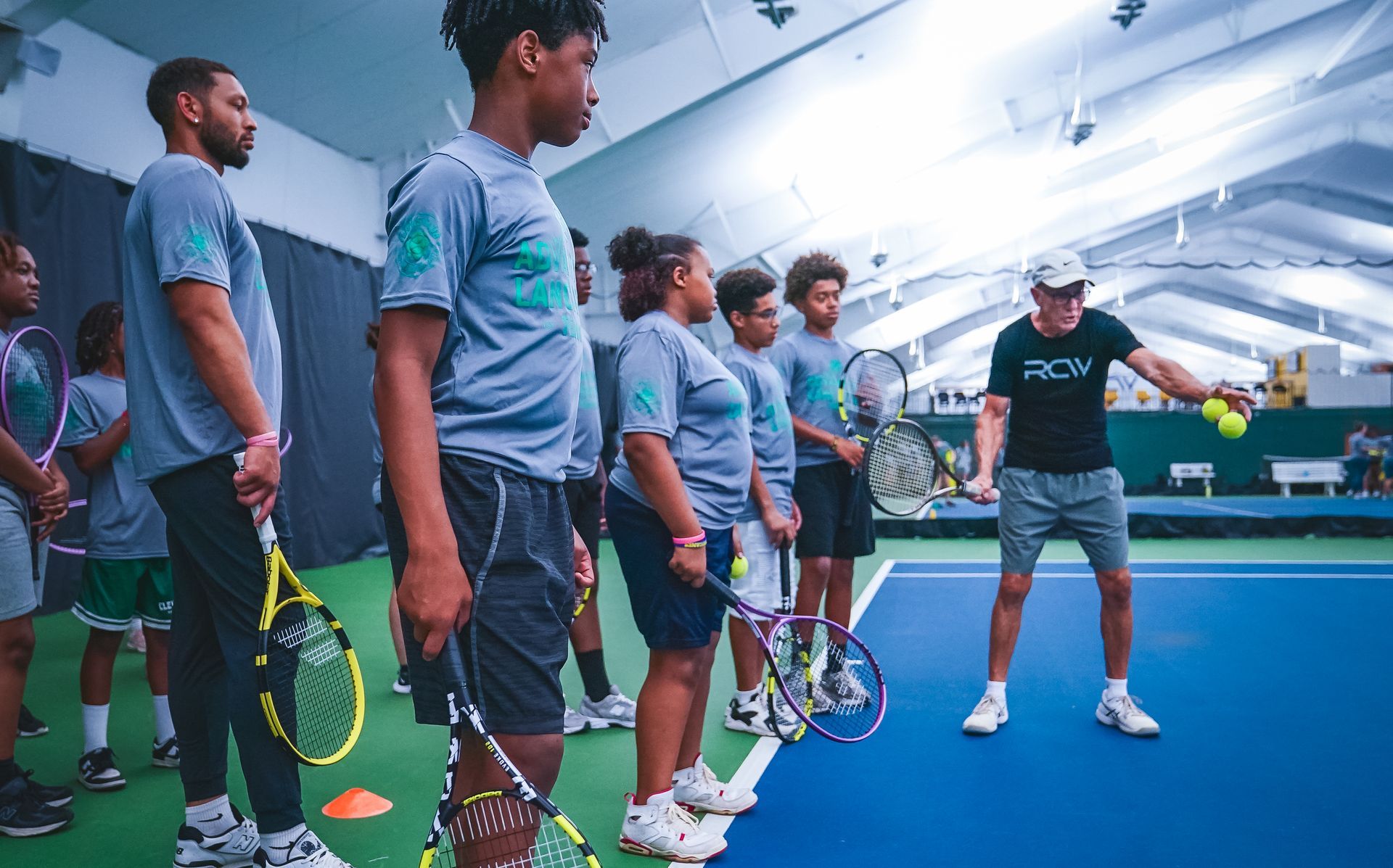 A group of people are standing on a tennis court holding tennis rackets.