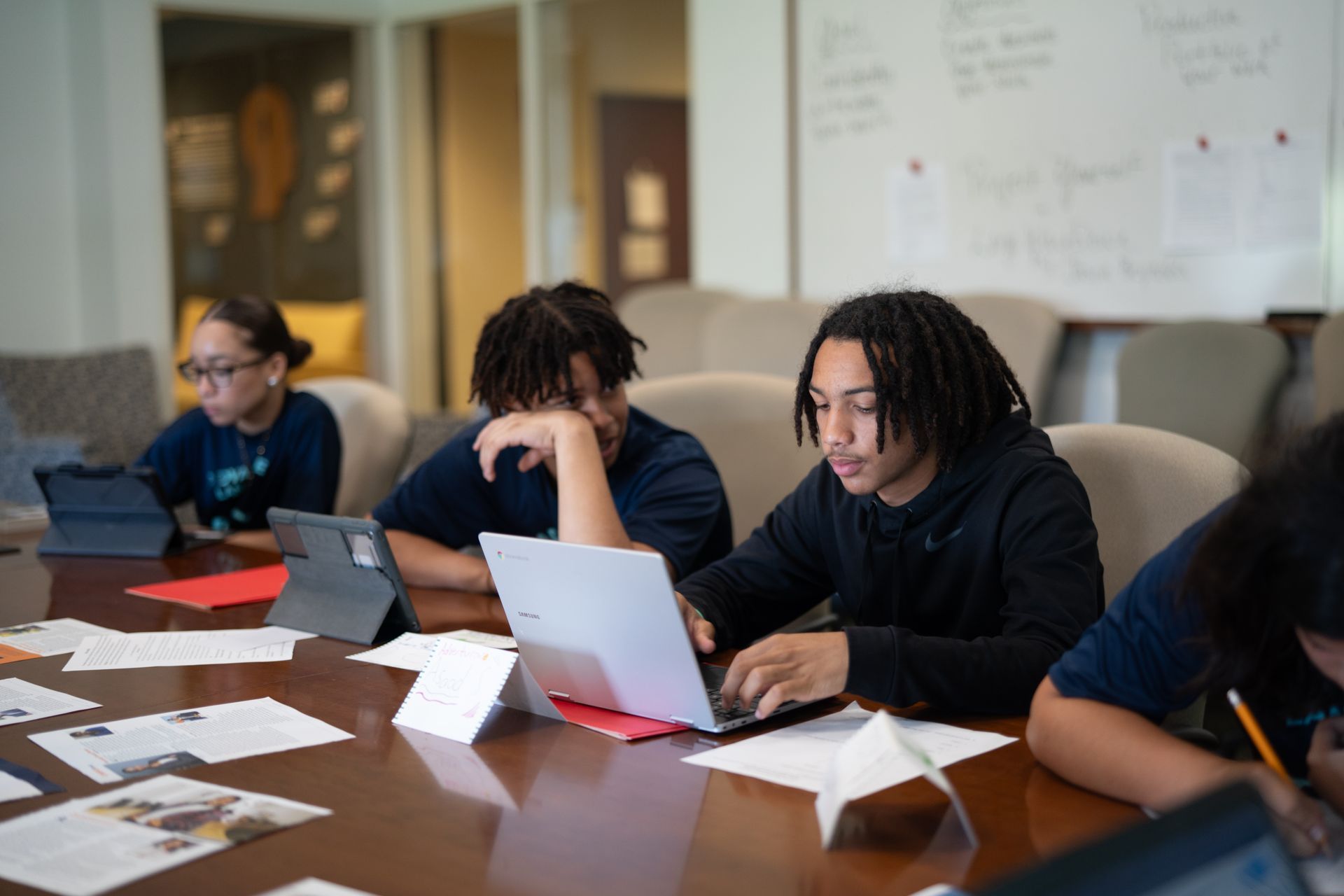 A group of young people are sitting at a table using laptops.